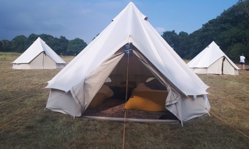 Close-up of a single bell tent in a field with its door open revealing orange pillows inside