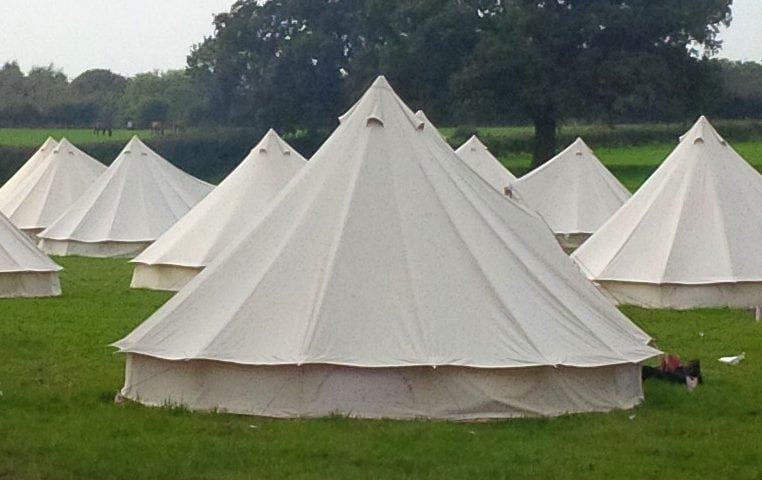 Wide pastoral shot of many white bell tents arranged in a field at a wedding