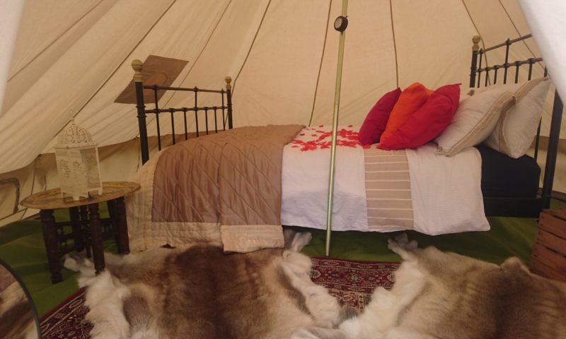 Bell tent honeymoon suite with antique iron bed, rose petals scattered on the quilt, Persian rug and Moroccan lanterns