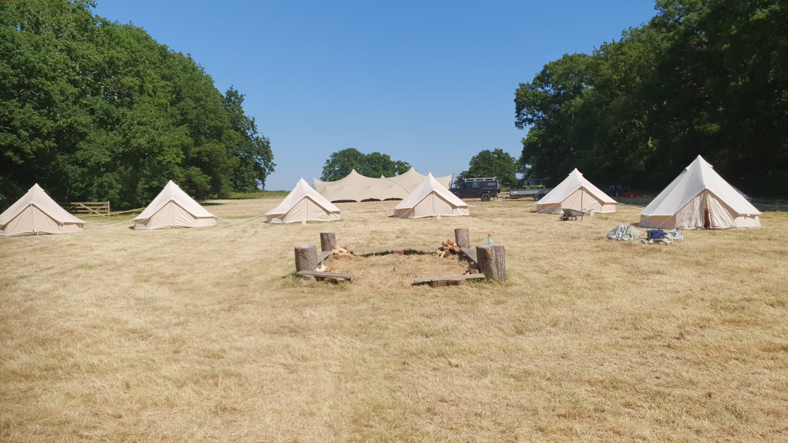 Bell tent village in an open field with pathways and trees in the background