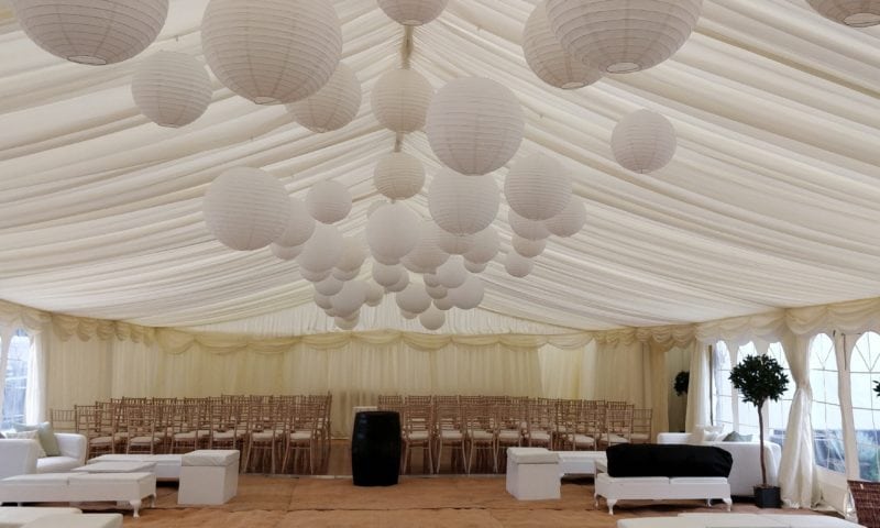 Traditional marquee set for a wedding ceremony — rows of chiavari chairs under dozens of large white paper lanterns