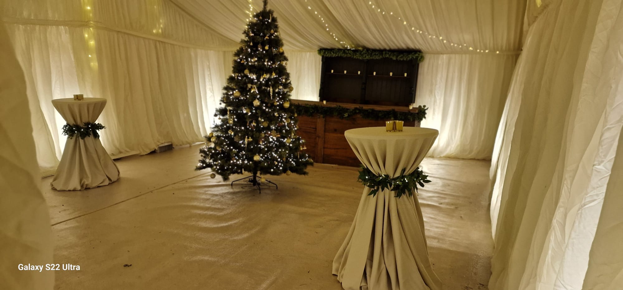 Cream-lined marquee interior with a Christmas tree, cocktail tables and warm fairy lights
