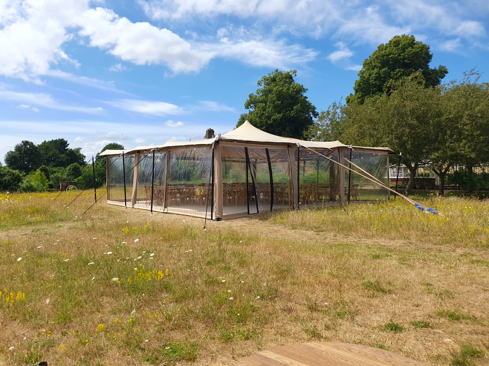 Clear-sided garden canopy with peaked roof sections in an open field on a bright day