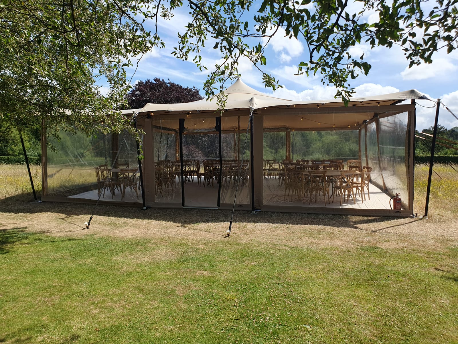 Clear-sided canopy in a garden orchard area with wooden picnic benches and dappled shade