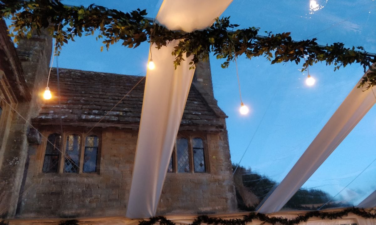 Looking up through a clearspan marquee clear roof at a Cotswold manor house against a deep blue sky at dusk