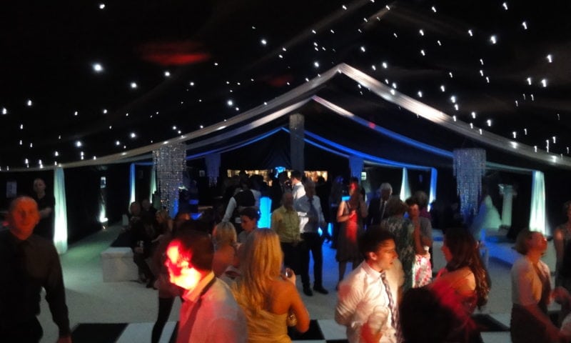 Clearspan marquee at night — guests dancing on a chequered floor under black star-cloth with fairy lights and blue uplighting