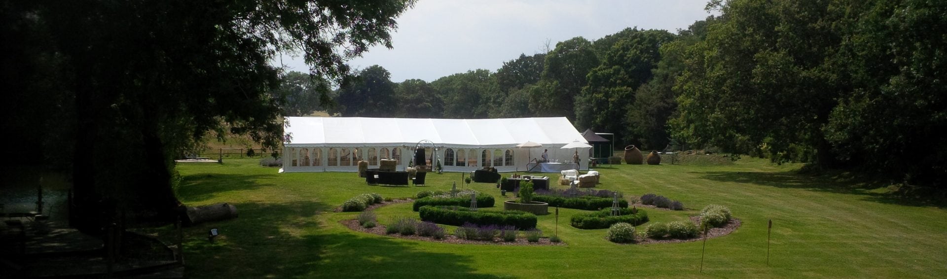 A clearspan marquee set in an exceptional estate garden with formal hedges and an ornamental pond