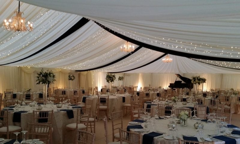 Clearspan marquee at night — ivory draping with black accent swags, fairy lights and crystal chandeliers