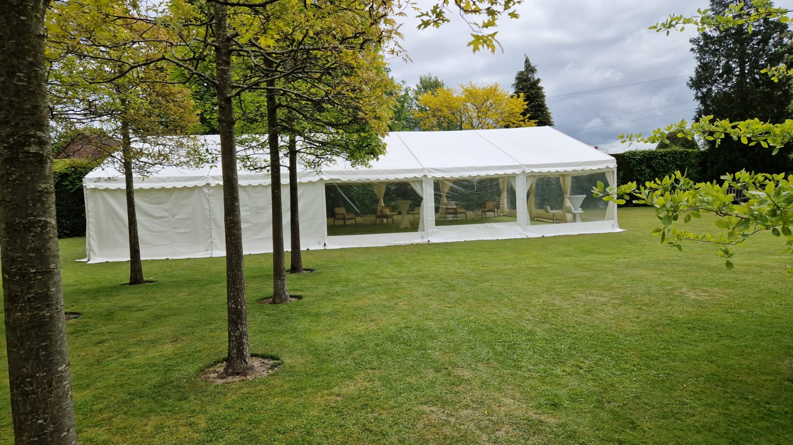 White clearspan marquee on a large lawn with transparent side panels and trees in the foreground