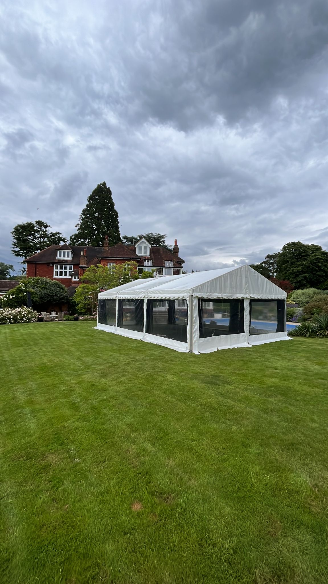 Portrait shot of a white clearspan marquee on a green lawn under dramatic cloudy skies