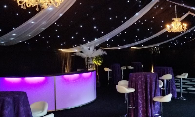 Corporate marquee interior at night with illuminated curved bar and crystal chandeliers