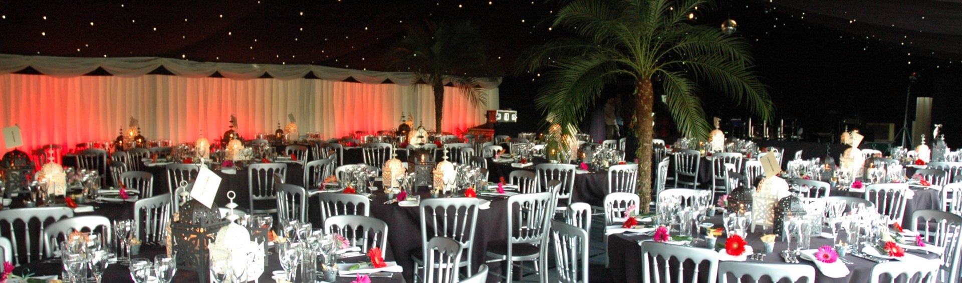 Corporate gala dinner inside a large marquee — black star-cloth ceiling, red uplighting and Moroccan lanterns