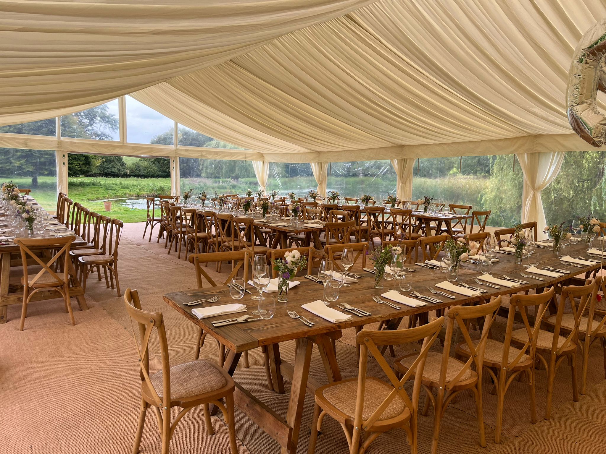 Cream-draped wedding marquee interior with long banquet tables, wooden chairs, place settings and a chandelier