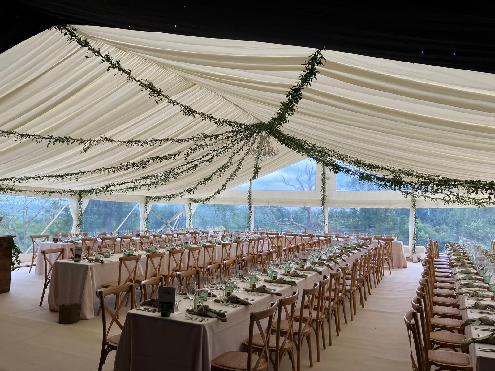 Cream-lined marquee interior with long banquet tables, greenery garlands and a black-lined ceiling section