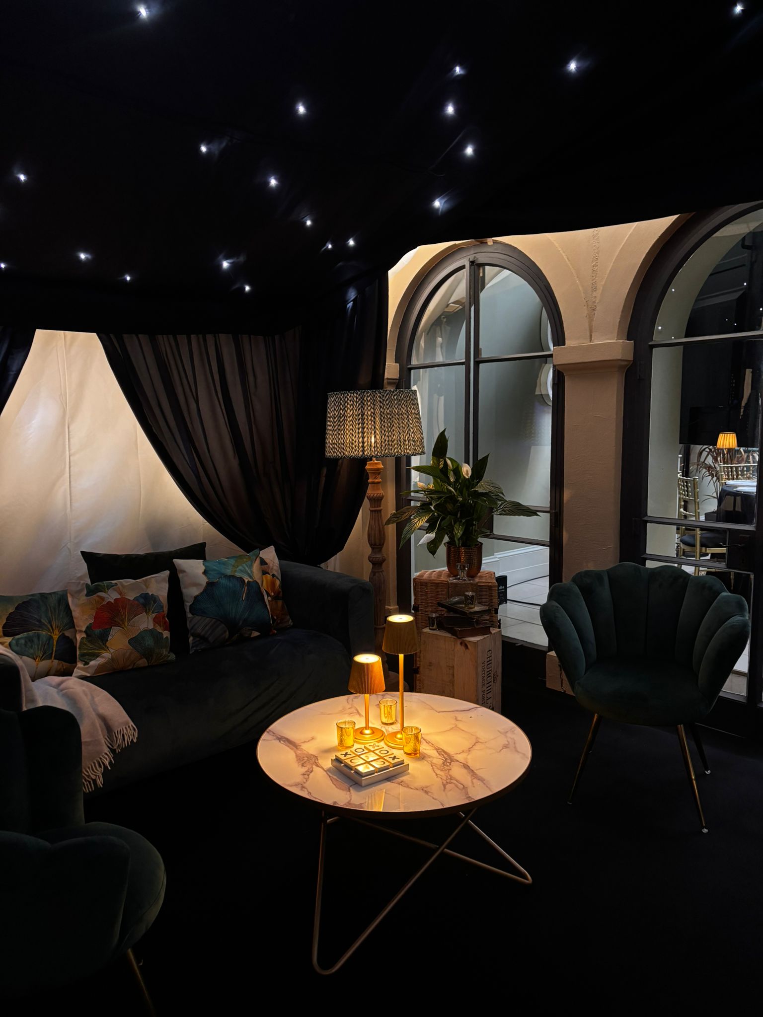 Intimate seating area inside a dark-lined marquee with starcloth ceiling, drapes, armchairs and warm table lighting
