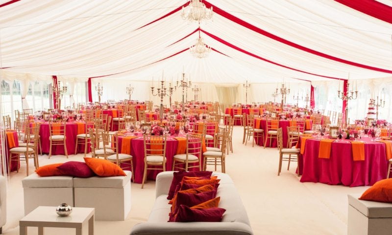 Colourful marquee interior with vivid red swag draping, chandeliers and gold chiavari chairs