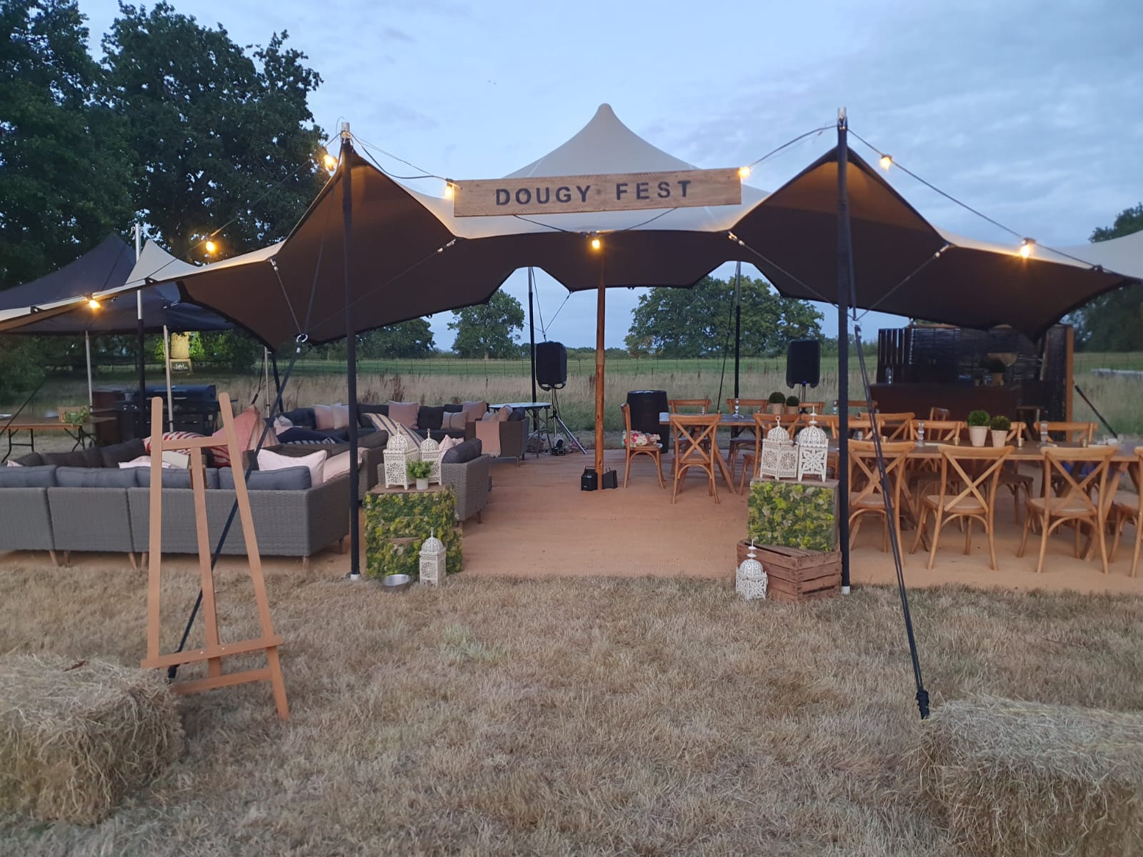 Festival-style stretch tent setup with seating, outdoor furniture and decorative props on dry grass