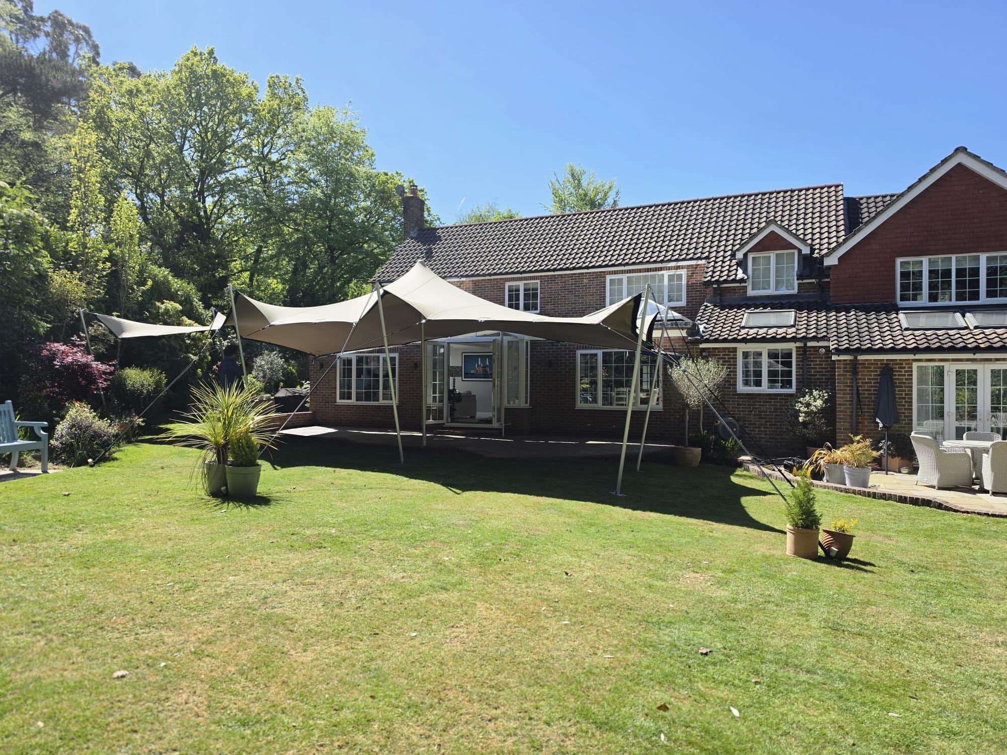 Garden marquee attached beside a house on a sunny lawn, with a small canopy extension and outdoor seating