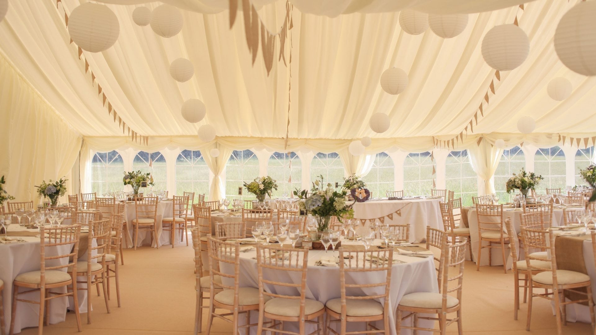 A traditional pole marquee interior with ivory pleated lining, lanterns and wildflower centrepieces