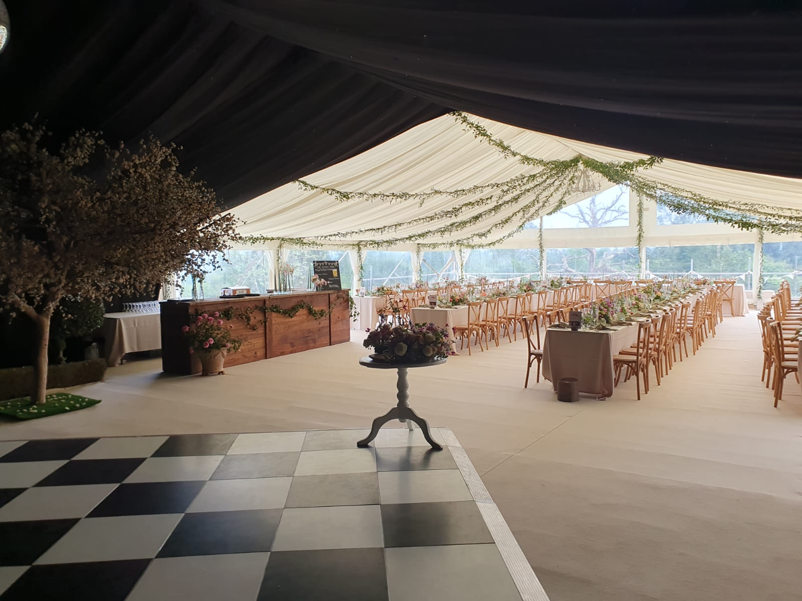 Large marquee interior with black-and-white dance floor, dark ceiling draping, bar area and long guest seating