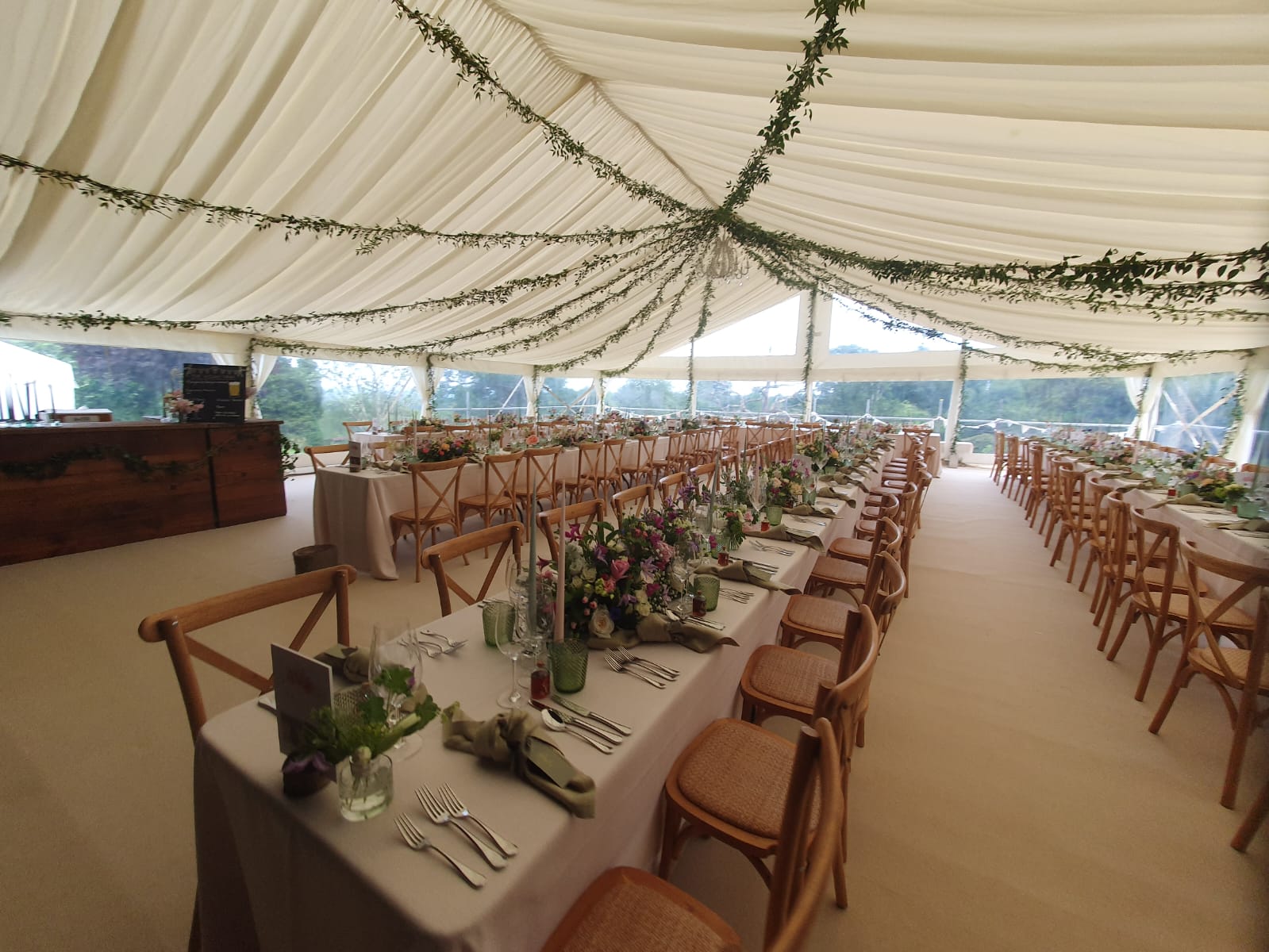 Large wedding marquee interior with long tables, wooden chairs, greenery and clear panoramic walls — Paul Simon Marquees