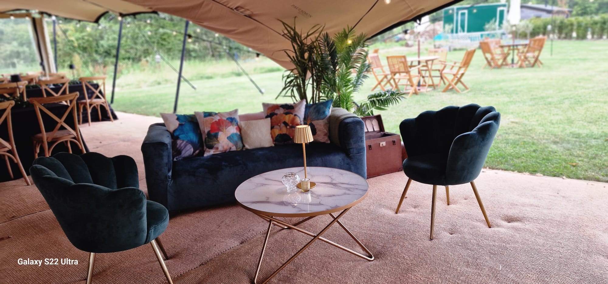 Soft lounge corner inside a marquee with sofas, armchairs, coffee table, cushions and plants