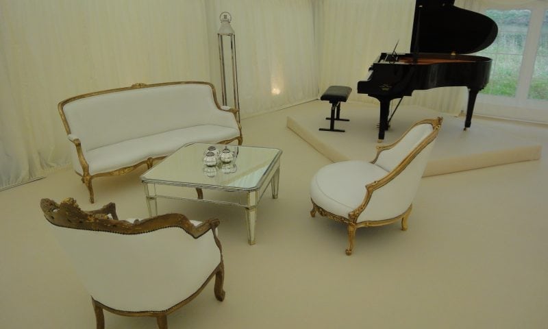 Ultra-luxurious marquee lounge with gilded Louis XV sofas, glass coffee table, grand piano and ivory carpet