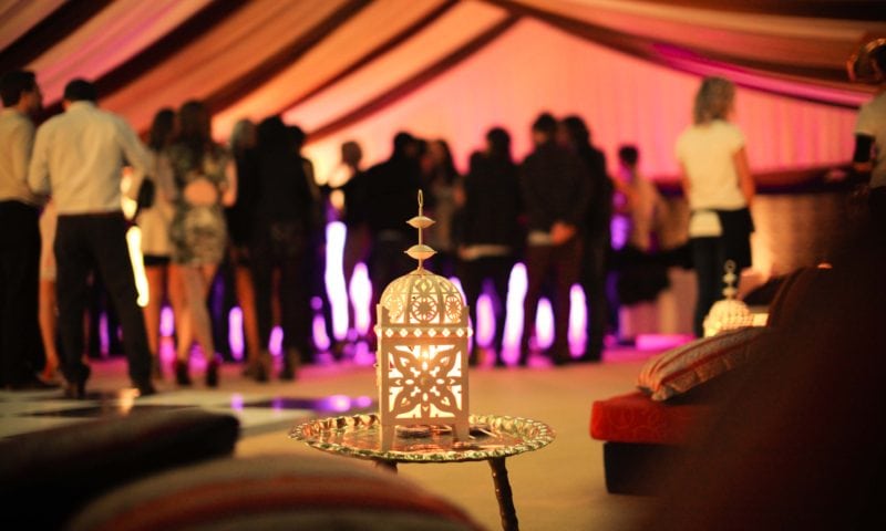 Close-up of an ornate white Moroccan lantern on a silver tray in the foreground of a colourful marquee interior