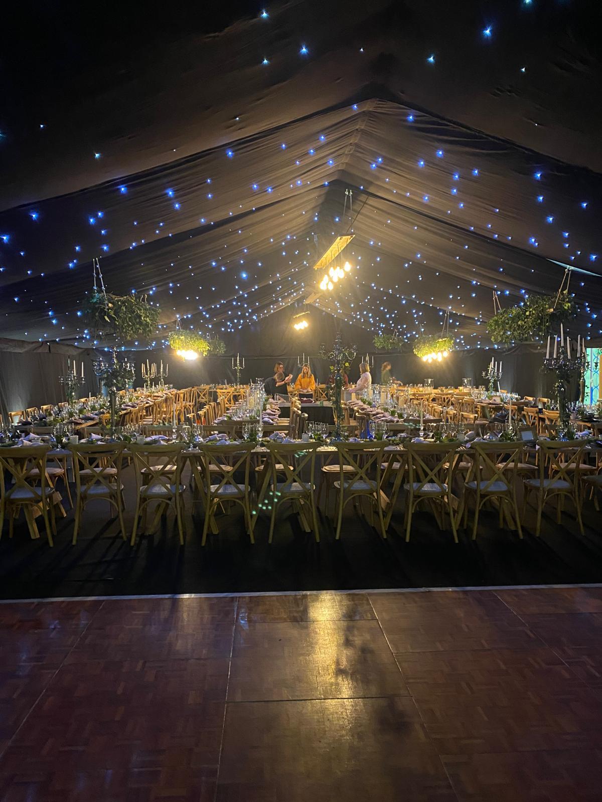 Long dining marquee at night with starry ceiling lights, rows of tables and a polished dance floor in the foreground
