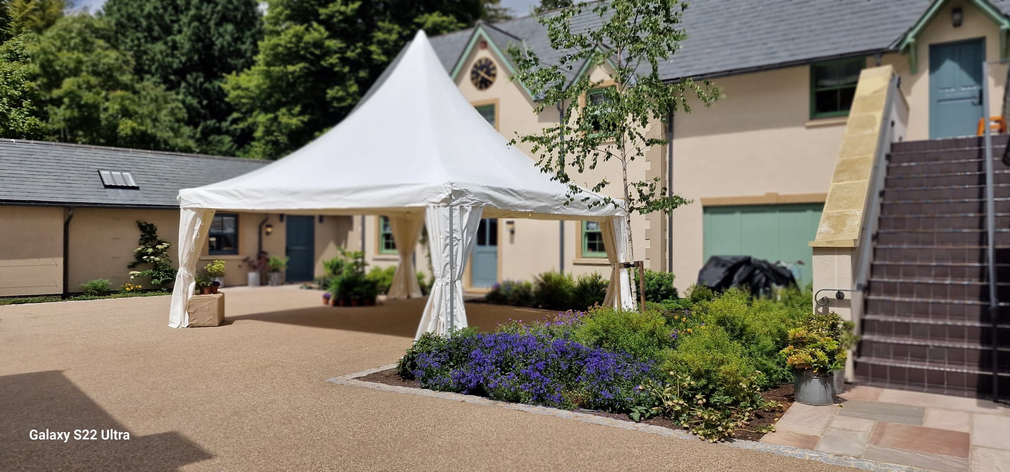 White pagoda-style entrance canopy outside a house with cocktail tables and stools arranged underneath