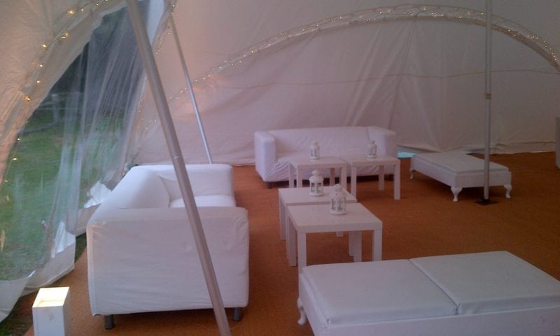 All-white pagoda marquee lounge — white sofas, cube ottomans, coffee tables and fairy lights strung on the arched frame at dusk