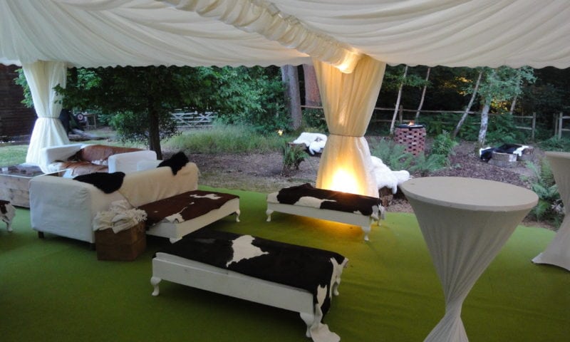 Pagoda marquee interior lounge area with white sofas, cowhide throw blankets and open-sided views into English woodland