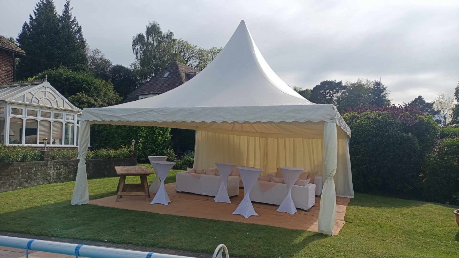 White pagoda canopy beside a garden pool or terrace, furnished with poseur tables and stools