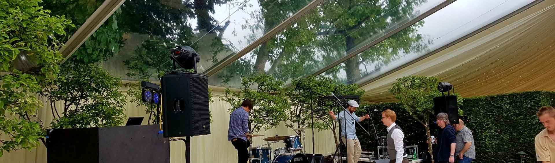Interior of a large clearspan marquee with a clear transparent roof at a summer party — a live band setting up inside
