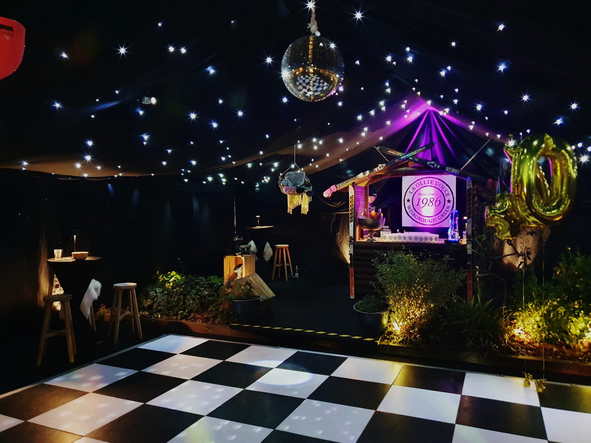 Night-time party marquee with starcloth ceiling, checkerboard dance floor, disco ball, stage lighting and themed decor