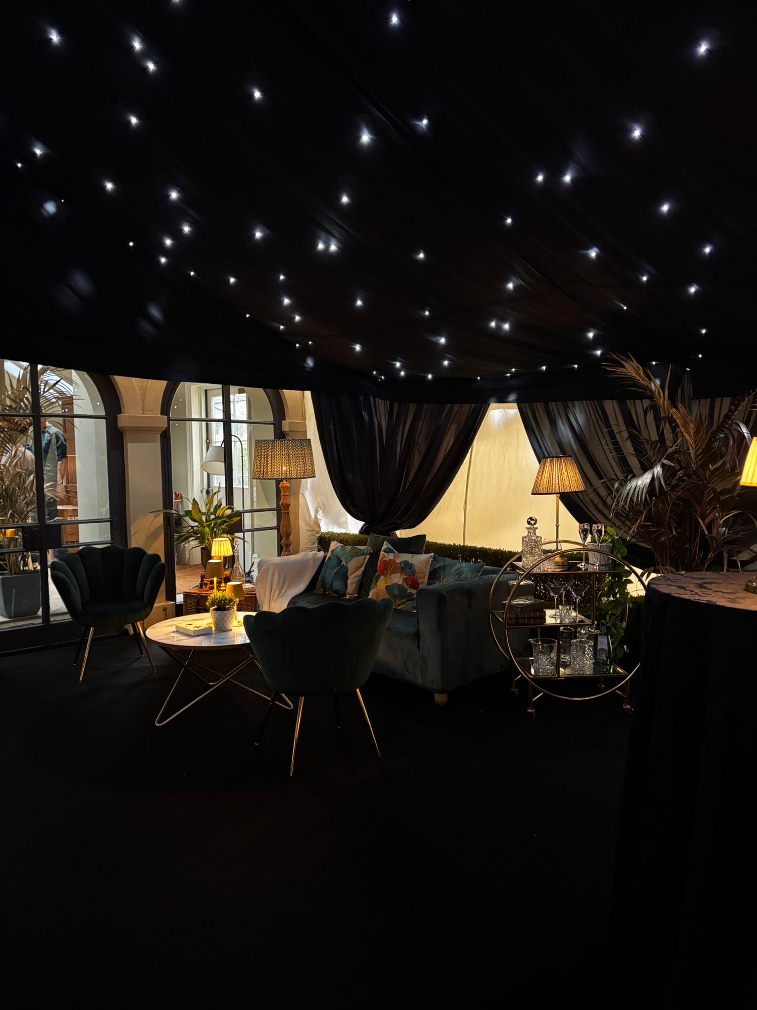 Interior lounge and dining setup under a black starcloth ceiling with small white lights and dark draping