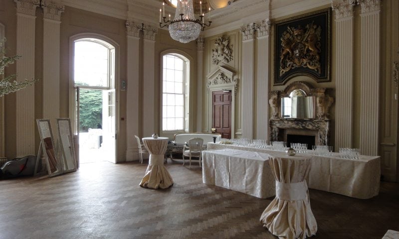 Interior of a stately home ballroom set for a drinks reception — champagne glasses and an ornate fireplace