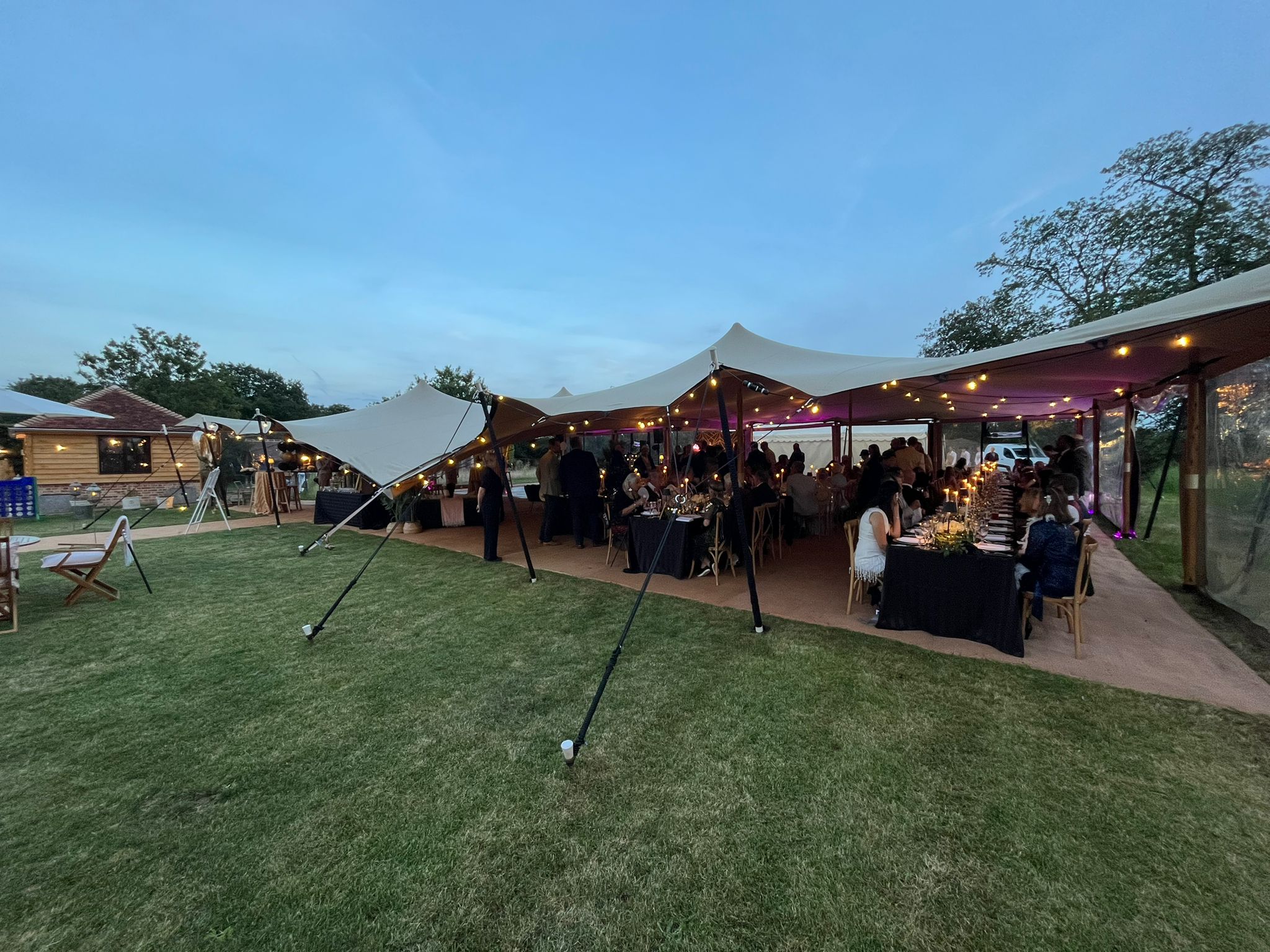 Evening stretch tent event with guests, warm lighting, clear sides and an open lawn approach