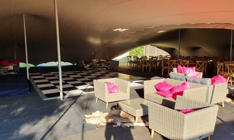 Interior of a stretch tent with grey and charcoal rattan chairs, hot pink cushions, a cowhide rug and a dance floor
