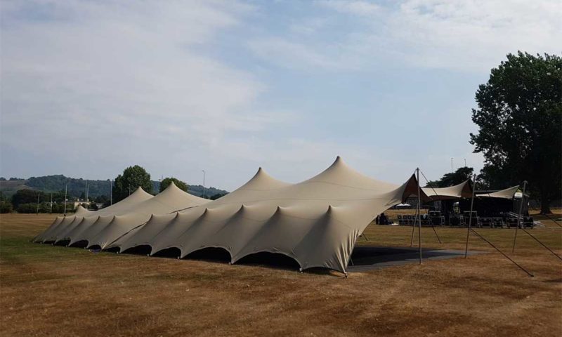 A very large stretch tent on a sports field showing its full scale with multiple peaks and stage equipment to the right