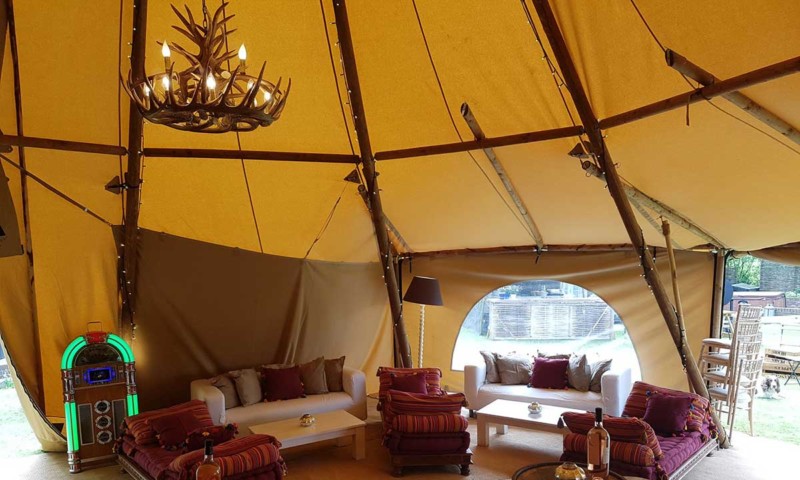 Tipi interior — an antler chandelier hangs at the peak with white and plum sofas and a retro jukebox