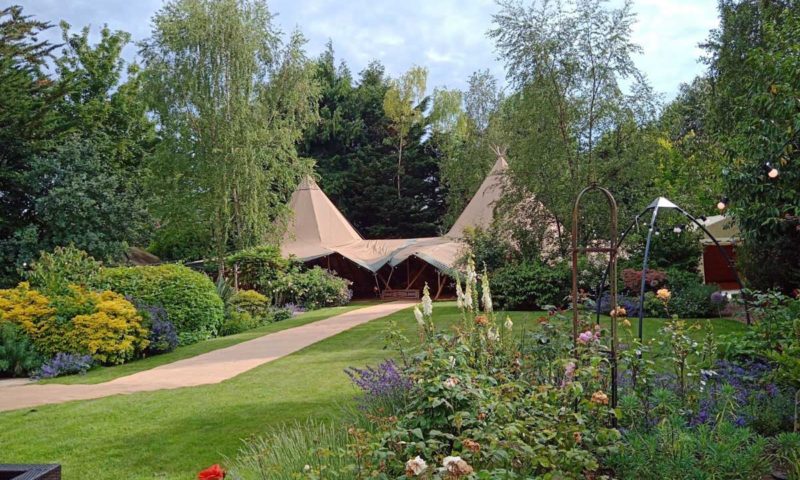 A double tipi in an English cottage garden accessed via a stone path through foxgloves and roses