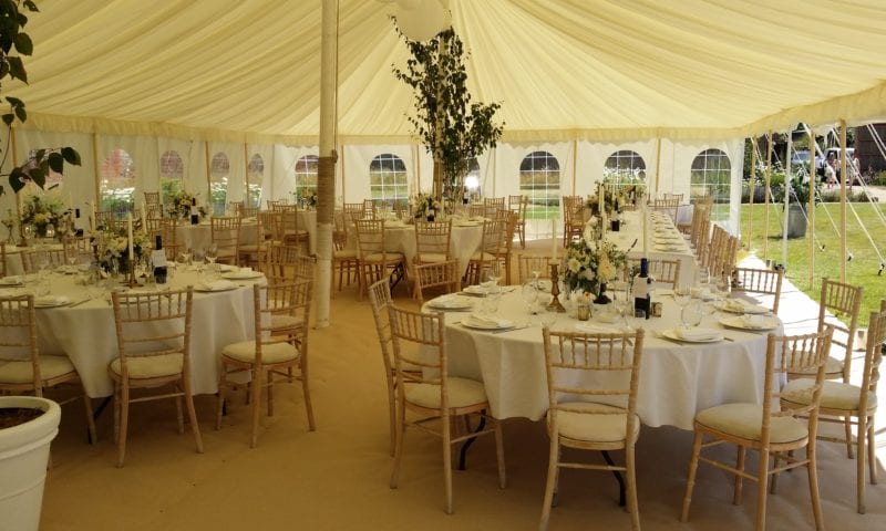 Traditional marquee interior with ivory pleated lining, round tables, natural wood chiavari chairs and birch trees