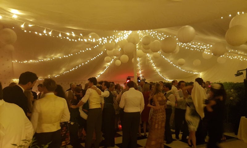 Wedding guests dancing inside a traditional marquee under ivory draping and fairy lights