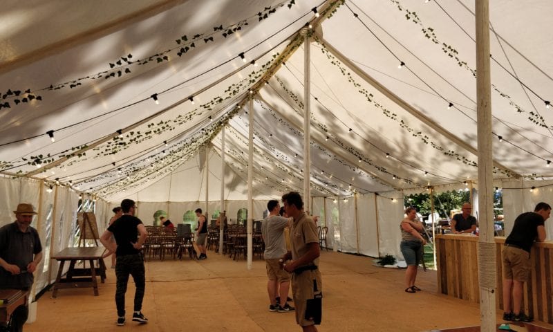 Interior of a traditional marquee with festoon and Edison globe lights entwined with ivy garland — bohemian festival feel