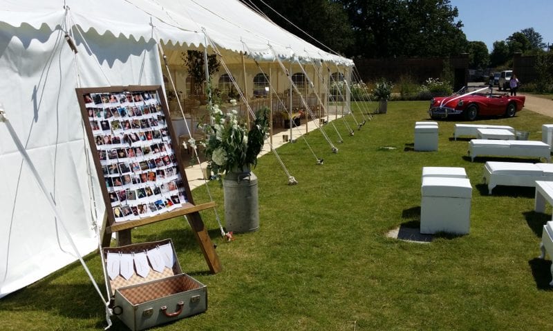 Traditional marquee with sides open — vintage red MG parked alongside, photo easel and galvanised milk churn on the lawn