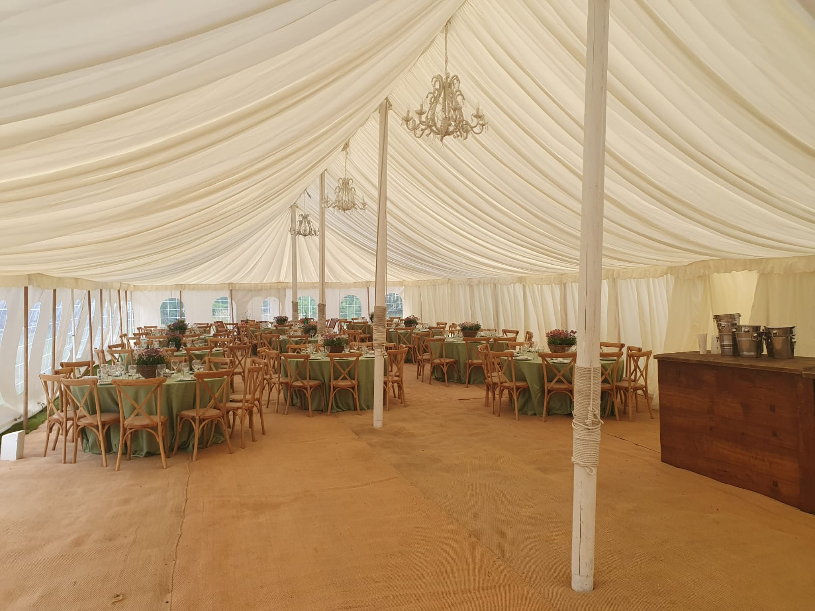 Traditional white-lined marquee interior with round tables, green chairs, floral centrepieces and a bar counter