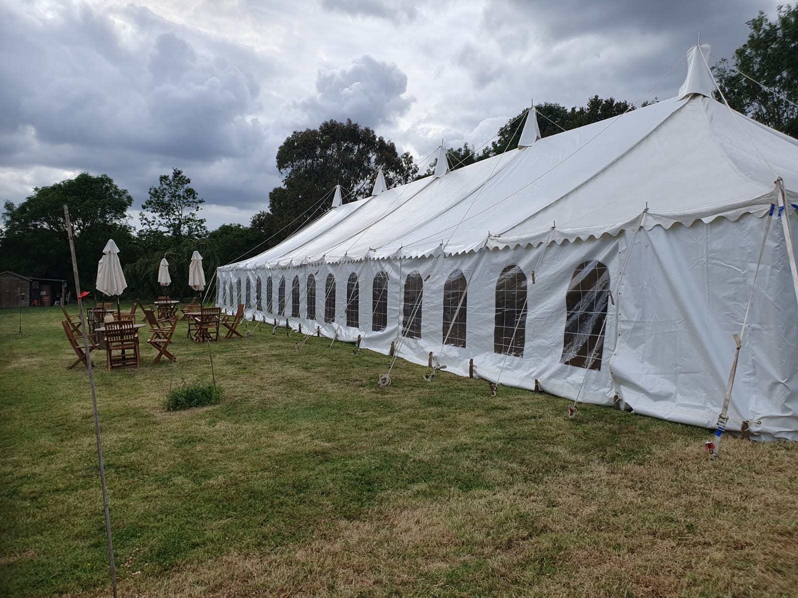 Exterior side view of a long traditional white marquee with arched window panels and outdoor seating nearby