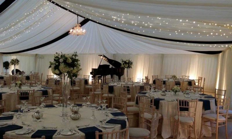 Traditional marquee at evening — ivory pleated lining with fairy lights, navy linen and silver mirror-ball centrepieces