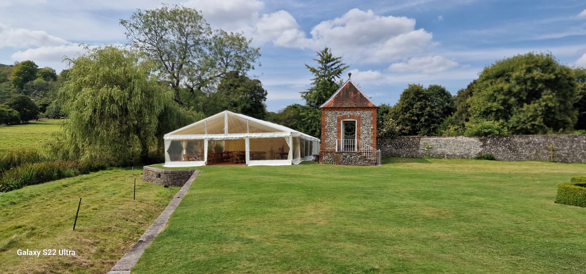 White garden marquee in a formal lawn setting beside a small brick building and paved path